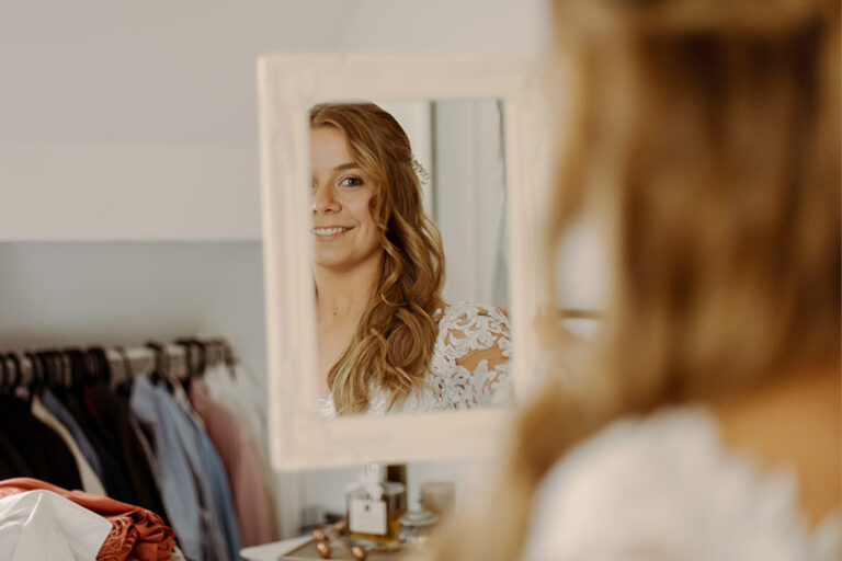 Bride-to-be in a wedding dress looking at herself in a mirror at a bridal shop.